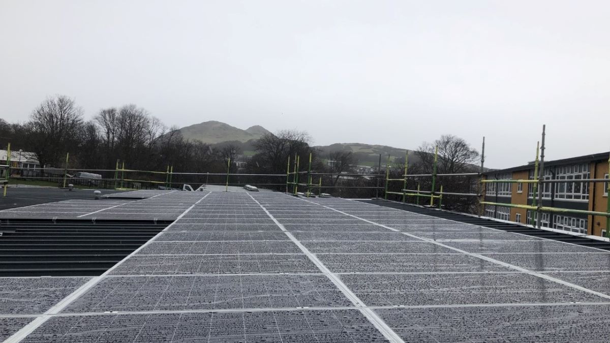 Solar panels being installed on the roof od a school in Scotland, surrounded by scaffolding.