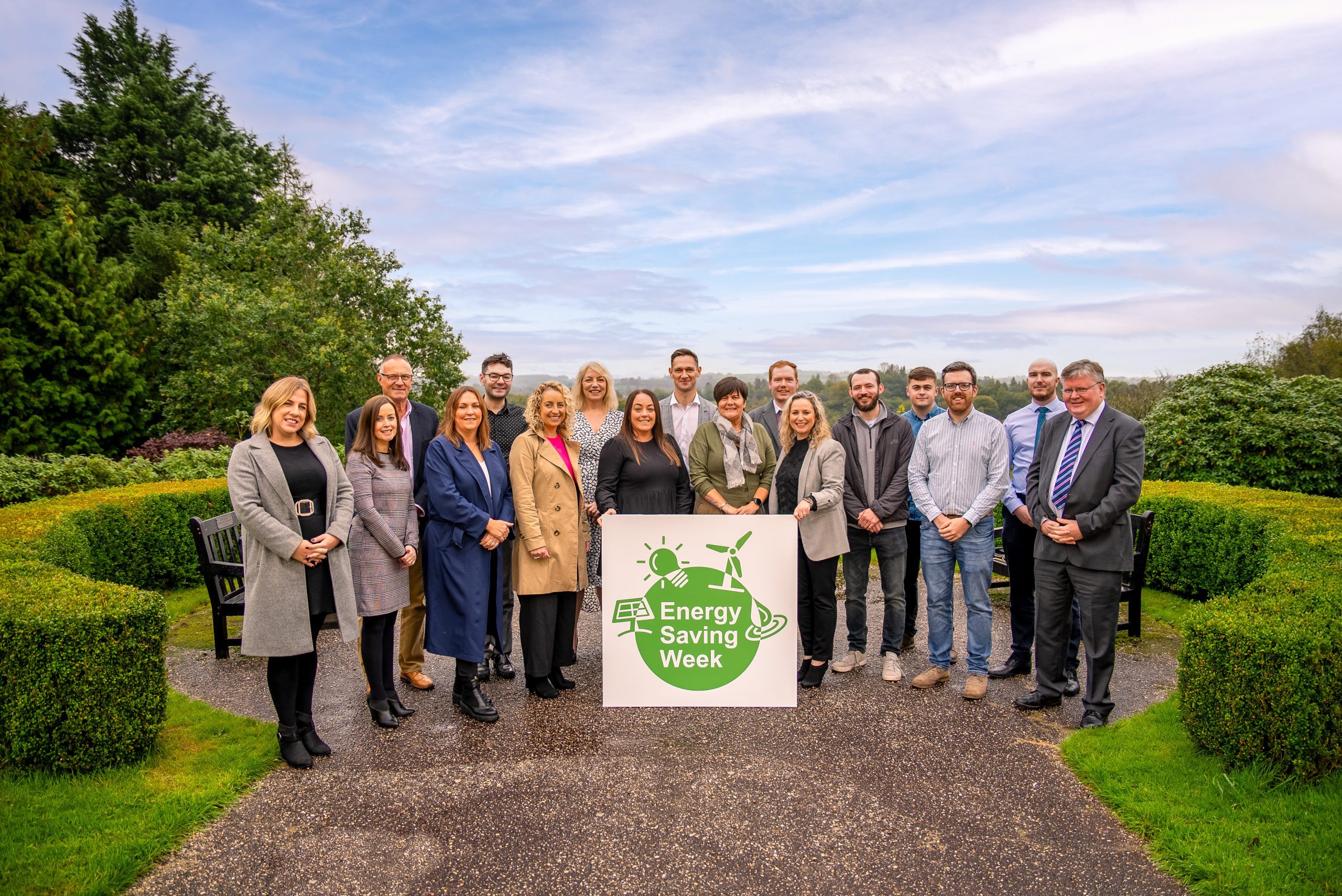 A group of people gathered around a sign with the Energy Saving Week logo.