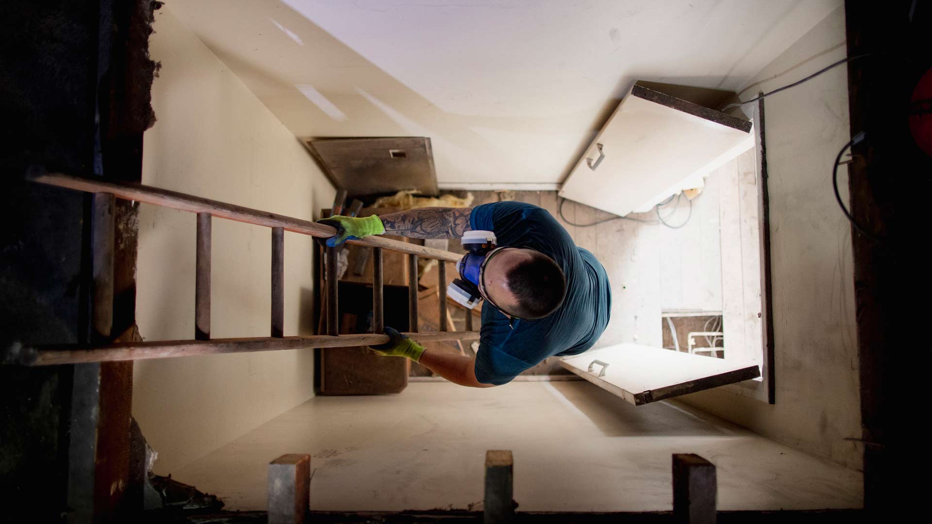 A man wearing PPE climbs a ladder into a loft.
