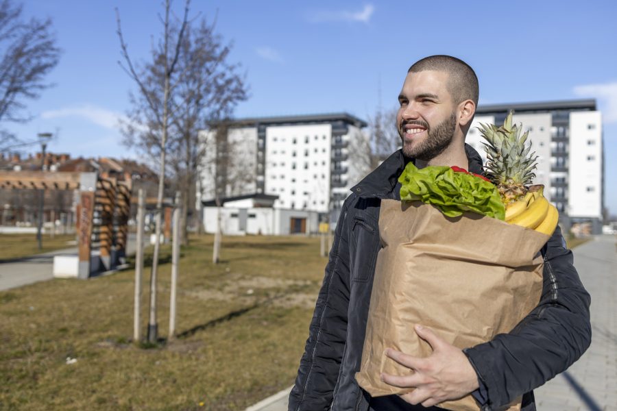 An individual carrying groceries while strolling home under a blue sky. 