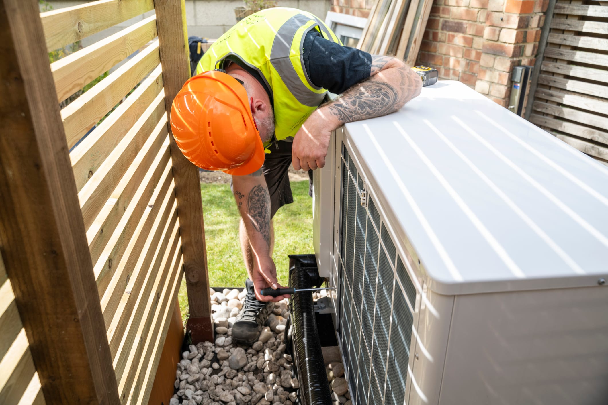 An electrician installing a heat pump in a garden on a sunny day.