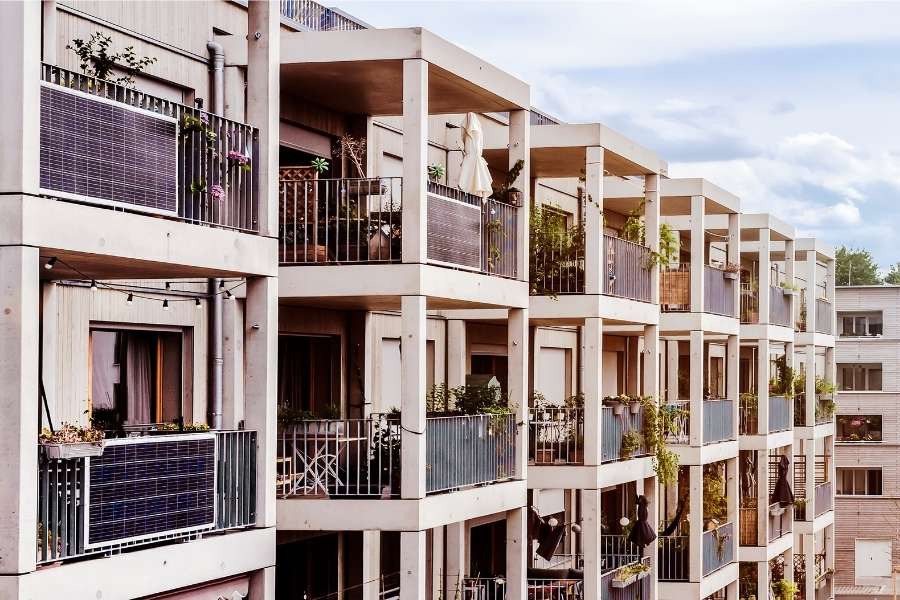 Plug-in solar panels installed on balconies of a German apartment building, with visible plants and outdoor furniture, showcasing residential solar energy adoption.