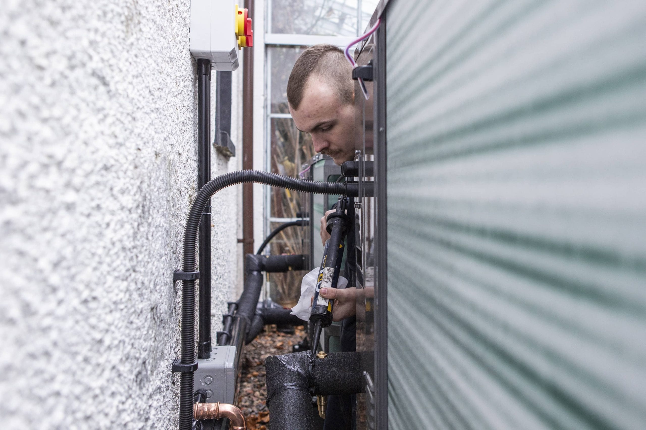 Installer insulates pipework at back of heat pump