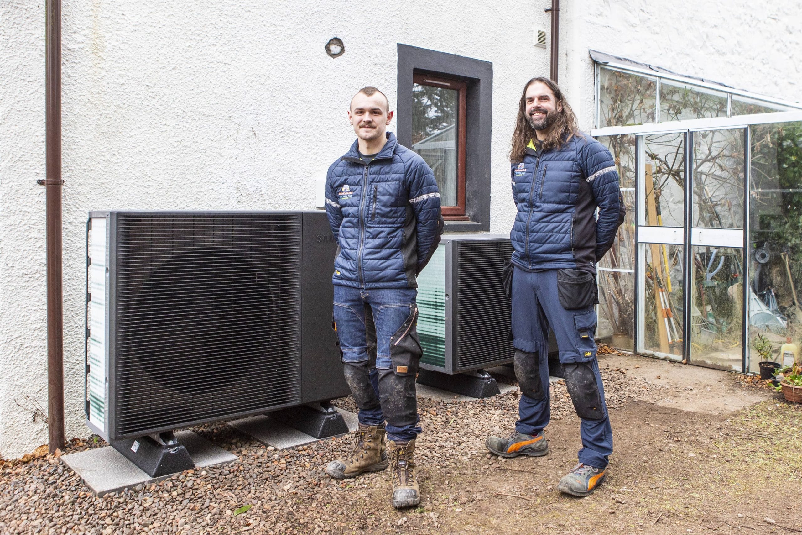 2 installers from stand in front of a black heat pump