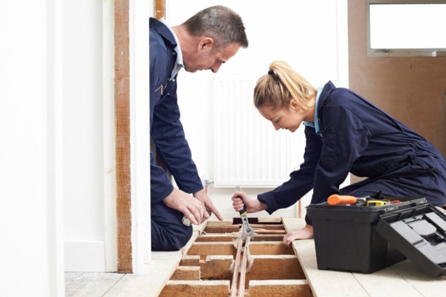 Tradesperson giving instructions to a trainee on working on piping in a home.